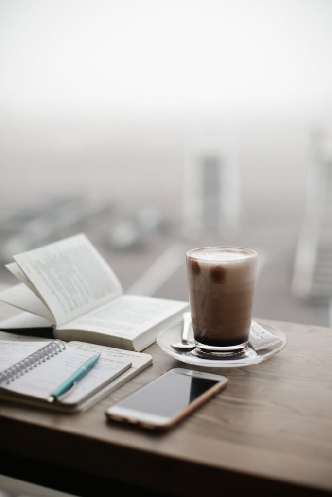 Contacto Cafetería Atlas Águilas A warm coffee sits beside a notebook and smartphone on a foggy day.
